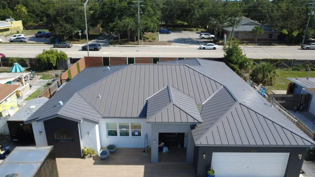 Aerial view of a modern home with a gray standing seam metal roof, white stucco exterior, and two-car garage